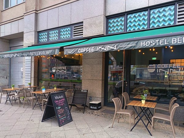 Außenansicht des Coffee INN Hostels mit Cafétischen auf dem Gehweg