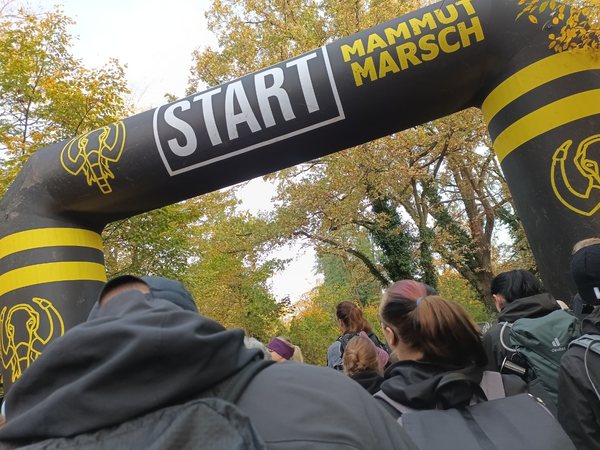 Startbogen des Mammutmarschs, davor wartende Teilnehmerinnen und Teilnehmer